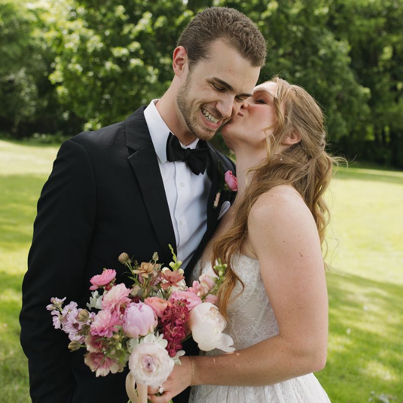 June bride and groom sharing a kiss with their flowers